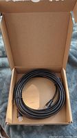 Black coiled RJ45 Cat-6 Ethernet cable in open brown cardboard box, showing cable connectors and packaging.