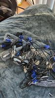 Photo showing a pile of 15 black VGA cables with blue connectors on a grey fabric surface