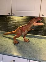 Side view of the Jurassic Park T. rex figure on a countertop under cabinets, showing its full length and detailed textures.