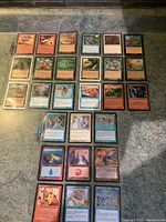 Top-down photo of 28 Magic The Gathering cards laid out in a 7x4 grid on a carpet surface, showing card fronts with colorful fantasy artwork and text.