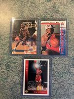 Three Michael Jordan basketball cards in plastic protective sleeves on a textured surface.