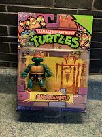 Front view of sealed Michelangelo action figure from Teenage Mutant Ninja Turtles with orange bandana, accessories in original carded packaging.