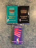 Photo of three sealed Skybox basketball card packs: teal Series II inaugural edition, black inaugural edition, and purple 1991-92 season pack.