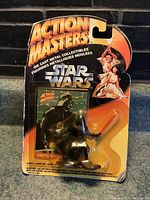 Front view of the sealed Star Wars Darth Vader diecast figure in original packaging, showing the orange and black card with 'Action Masters' at the top and character art, figure visible through bubble with some wear on package and burst bubble area.