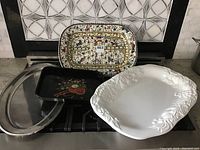 Five large platters on a stove, showing metal and ceramic materials with decorative designs and patterns.