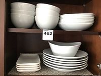 Photo showing a collection of white ceramic dinnerware arranged on shelves including bowls, round plates, and rectangular plates.