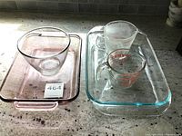 Photo showing two rectangular glass baking dishes stacked, one clear and one with pink tint, with a clear glass mixing bowl and two Pyrex measuring cups on top.