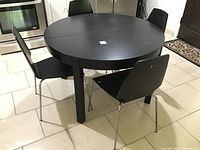 Black round IKEA BJURSTA table in retracted round form with four black VILMA chairs surrounding it. Table shows wear.