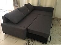 Side view of the dark grey fabric sectional couch with cushions. Sectional shows chaise and part of pull-out bed extended with storage visible underneath.