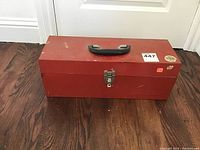 Closed red metal tool chest with handle and latch on hardwood floor