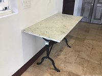 Full view of the rectangular stone top table placed against a wall indoors on a tiled floor.