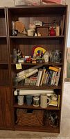 Front view showing five shelves containing books, decorative items, rolled papers, and storage baskets.