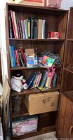 Bookshelf photo showing multiple shelves filled with books, small toys, and miscellaneous household items. Minor wear visible on shelf edges and corners.