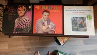 Three vinyl record albums on a wooden surface: Patti Page, The Best of Jim Reeves, and Sammi Smith's Help Me Make It Through the Night.