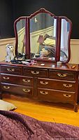 Wooden dresser with tri-fold mirror attached, brass hardware, showing front view and surface scratches.