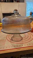 Front view of glass pedestal cake server with transparent ribbed dome lid and round knob.