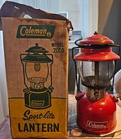 Red Coleman Model 200A Sport-Lite lantern standing next to original cardboard box with printed label and illustration.