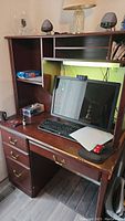 Full view of wooden desk with computer monitor, keyboard and mouse placed on top. Shows top shelving section and side compartments.