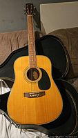 Full view of Westville acoustic guitar with natural wood finish, six steel strings, black pickguard, and case partially visible