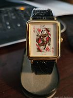 Front view of rectangular lady's wristwatch with Queen of Hearts playing card design on the face, black textured leather strap, gold-tone bezel.