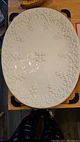 Large oval serving platter with embossed floral design on white ceramic, photographed on a wooden table.