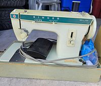 Side view of Singer sewing machine on base with foot pedal and spool of thread loaded.