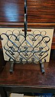 Wrought iron magazine holder with decorative curved design and handle on wooden surface