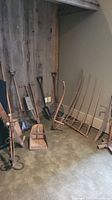 View of multiple antique tools leaning against wall including shovels, rakes, and thatcher