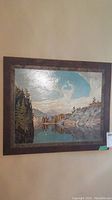 Both framed prints as seen hanging on a wall, showing full view of one artwork depicting a lake scene with rocky cliffs and trees.