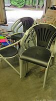 Set of stackable chairs with silver metal frames and black plastic seats and backs seen in storage or warehouse setting.