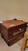 Overall view of the vintage wooden chicken incubator showing its rectangular shape, wooden slats on top, legs, front door with window and white knob.