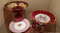 Painted glass footed bowl, pink china plate, hand-painted shell-shaped bowl with floral decoration and gold trim, plus three small red glass items.