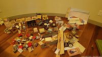Wide shot of multiple dollhouse furniture pieces spread on the floor including chairs, tables, shelves, and various accessories.