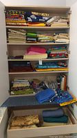 Photo of shelving unit with neatly folded fabrics in multiple colors and patterns, books and paper patterns on shelves and a drawer with more fabric.
