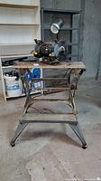 Wordsmith bench grinder with attached lamp mounted on Black & Decker Workmate portable workbench, set in basement environment.