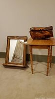 Photo showing wooden framed mirror with shelf, small wooden table, and wooden carved trunk on top of table and leaning against the wall.