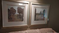 Photo of two wood framed prints hung above a sofa, showing both artworks fully framed and matted behind glass.