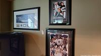 Three framed sports memorabilia items displayed on a wall: Curtis Joseph limited edition signed poster, Wayne Gretzky and Gordie Howe framed photo, and maple leaf stadium panoramic photo with pins.