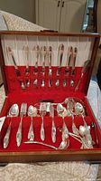 Opened box showing full cutlery set arranged in red velvet compartments with spoons, forks, knives, and serving pieces.