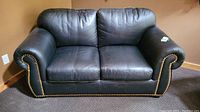 Front view of black leather two-seat sofa with rolled arms and brass nailhead trim