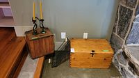 Full view of two vintage wood boxes, wire basket, and candle holders with candles placed on floor next to stone wall and wood floor