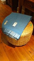 The blue Kenwood wool blanket draped over the basket weave ottoman showing overall color and texture.