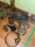 Group of brass and silver plated items including horn, silver serving dishes, thermometer, and fireplace tools on wooden floor.