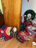 Overall grouping of Christmas quilts, Santa figures, gift bags, and wreath by wooden cabinet.