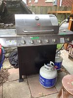Front view of Terr Gear 5-burner gas BBQ grill with three propane tanks in front, control knobs visible, cover partially visible underneath.