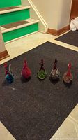 All five blown glass roosters displayed side by side on a black carpet near green stairs.