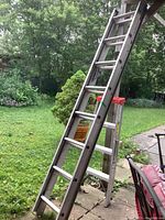 Wide view of two aluminum ladders set outside near patio and greenery.
