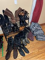 Photo showing various pairs of ladies boots and shoes arranged on and around a black metal shoe rack along with black and white patterned packing material.