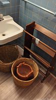 Photo of two large round wicker baskets and one smaller rattan basket inside a larger basket, positioned near a bathroom sink on a gray flooring.
