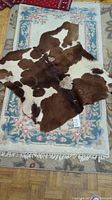 Cowhide rug on top of floral area rug with blue border and fringe